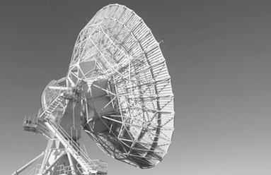 A radio telescope dish on its mount, tilted against a plain sky, in black and white.